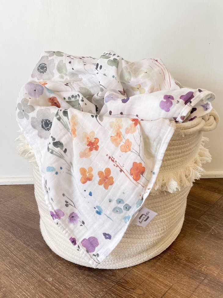 image of swaddle blanket draped over woven basket, blanket is white with floral print.
