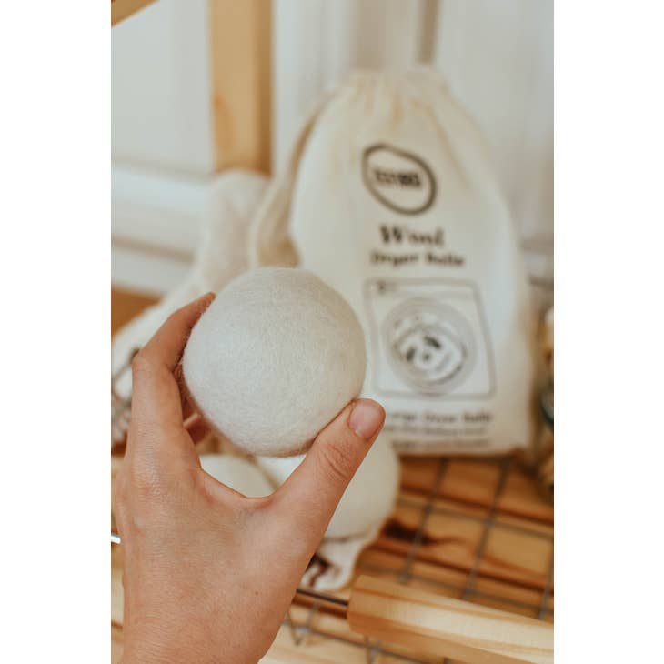 image of hand holding wool dryer ball, in the background there is a bag in which the set of wool dryer balls come in