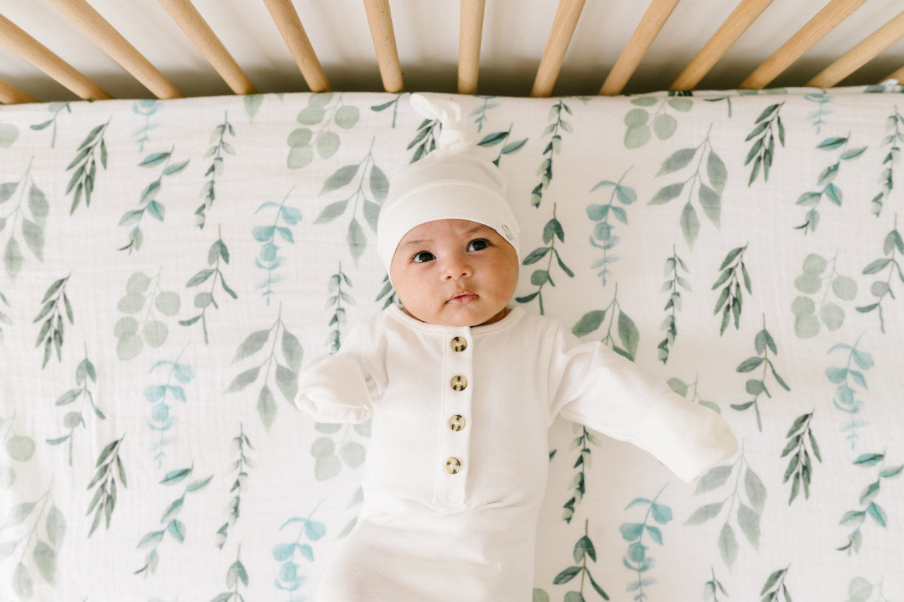 image of infant laying on white muslin swaddle blanket with leaf printwith