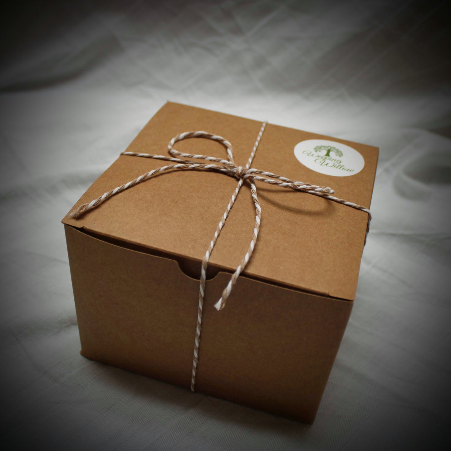 Image of kraft cardboard gift box with string tied around, weeping willow logo sticker on top.