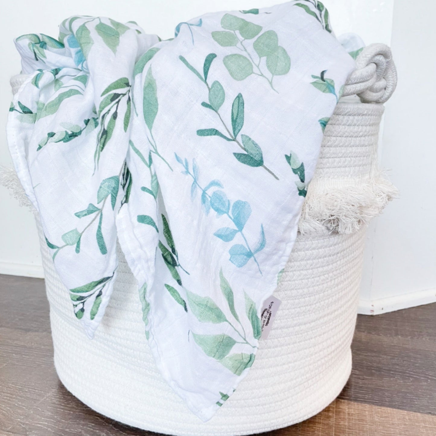 image of white muslin leaf printed swaddle blanket draped over basket