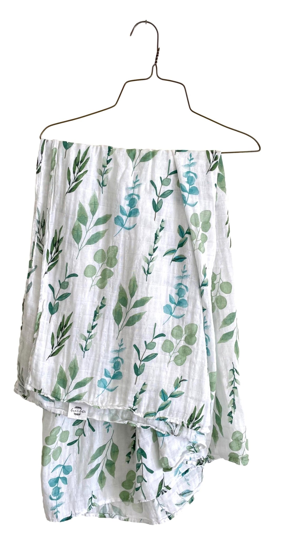 image of white leaf printed cotton muslin baby swaddling blanket hanging on a hanger