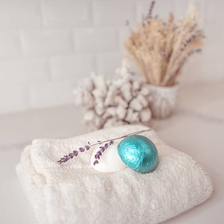 image of shower steamers sitting on a towel. One steamer is in product packaging, the other is unwrapped.