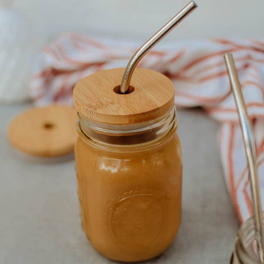 Image of mason jar with filled with drink or soup, has a bamboo lid. Bamboo lid has a hole for a straw, stainless straw is in the  lid hole.