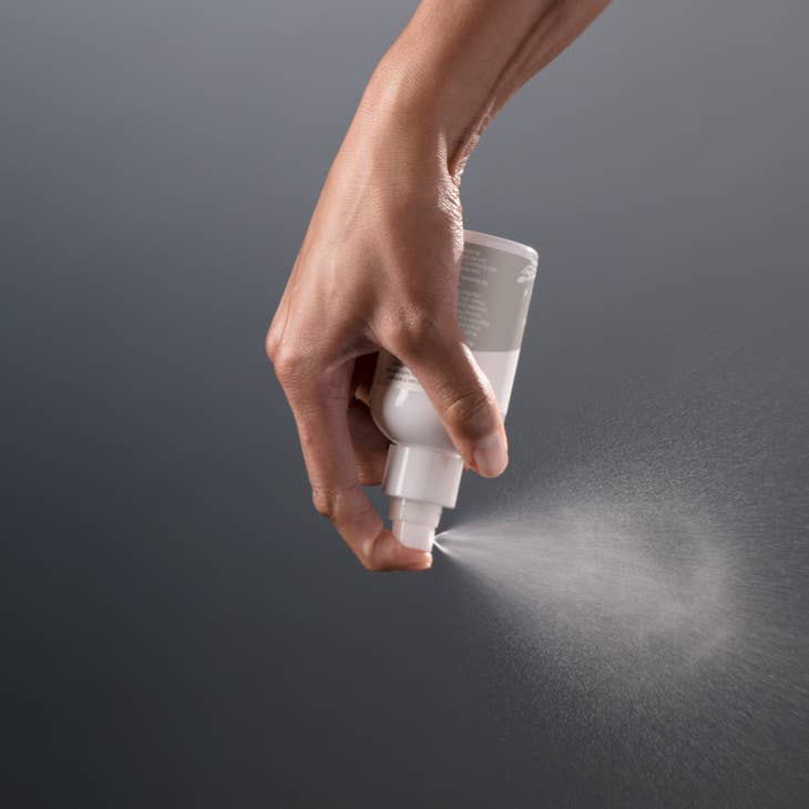 image of hand holding bottle of perineal spray upside down while spraying, mist coming out of bottle