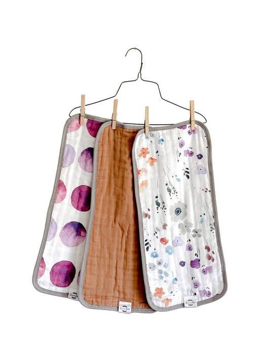 image of 3 organic cotton muslin burp cloths hanging on a hanger, one solid, two have watercolor print fabric.