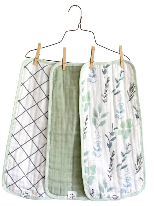 Image of three organic cotton muslin burp cloths with different prints, with sage accent colors, shanging on hanger. 