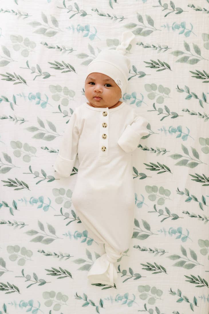 image of infant wearing white knotted gown and cap