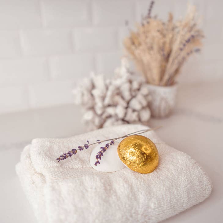 image of product on a towel. one shower steamer is unwrapped, the other is in yellow foil product packaging. 