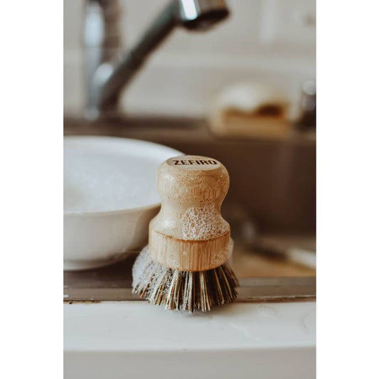 image of sudsy pot scrubber made from bamboo and palm fiber, kitchen sink in the background of image.