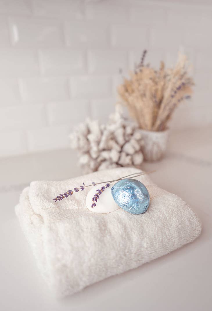 two shower steamers on a towel, one unwrapped, the other wrapped in blue foil packaging.