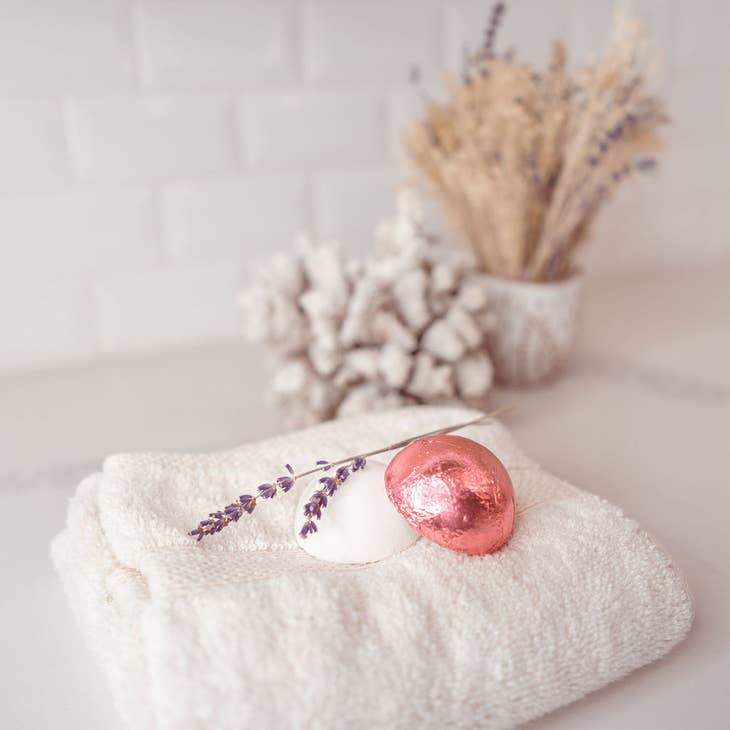 two shower steamers on a towel, one is wrapped in pink foil packaging