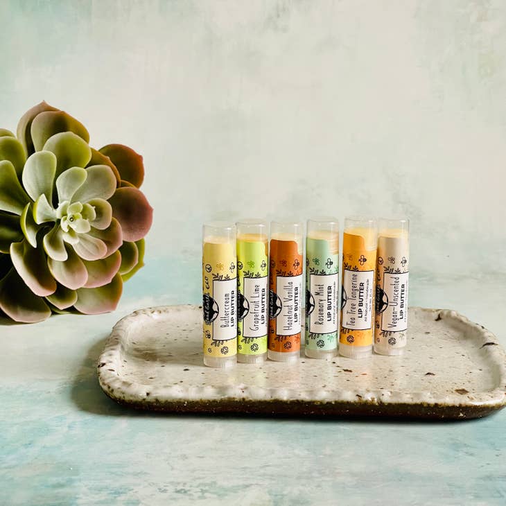 Image of lip balms in various flavors, hazelnut vanilla, buttercream, rosemary mint, tea tree tangerine, grapefruit lime.